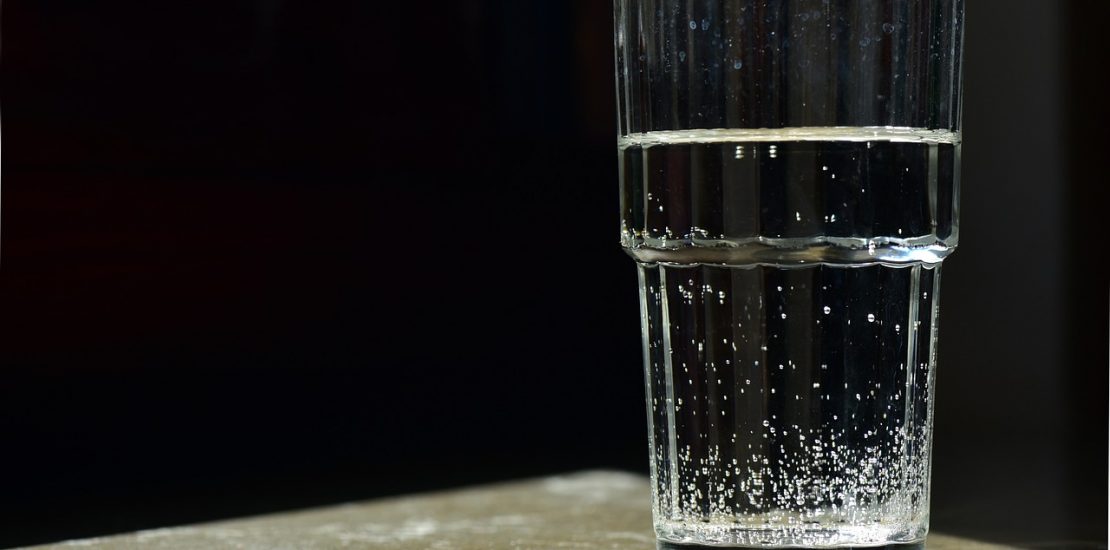 a clear glass of water sits on a table with a black backdrop